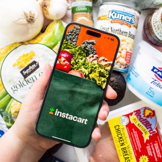 A person holding up a phone with groceries on it.