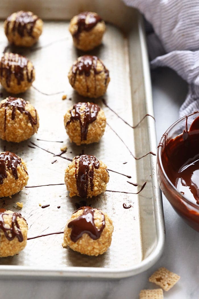 Crunchy no bake peanut butter balls drizzled with chocolate on a baking sheet