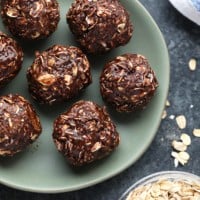 Cocoa oat balls decorated with peanut butter, placed on a plate alongside a bowl of oats.