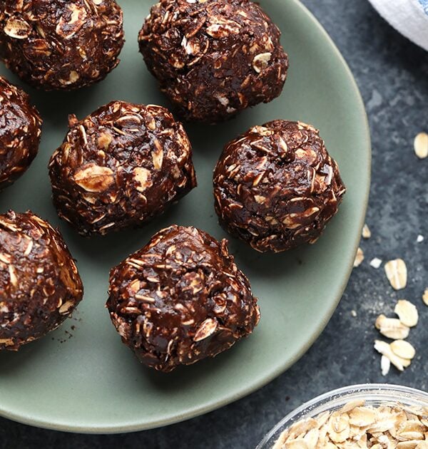 Cocoa oat balls decorated with peanut butter, placed on a plate alongside a bowl of oats.