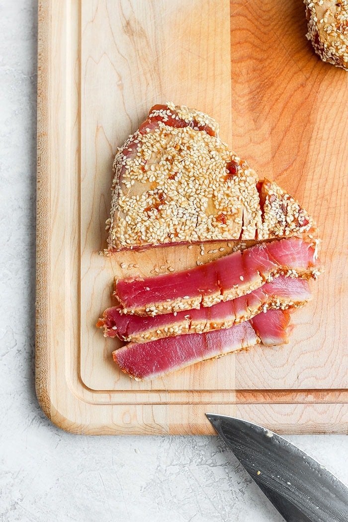 You are going to love this simple seared ahi tuna recipe. It's marinated in soy sauce, ginger, and lime juice and then coated with sesame seeds. seared ahi tuna steak on a cutting board.