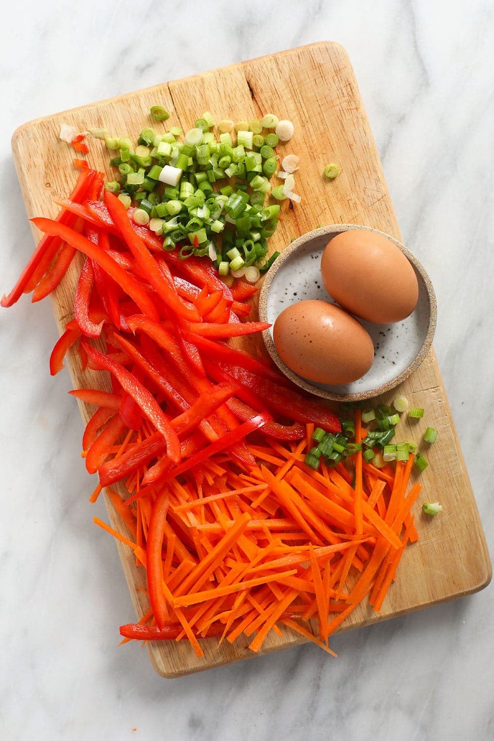 Green onion, red pepper, eggs, and carrots on a cutting board. 
