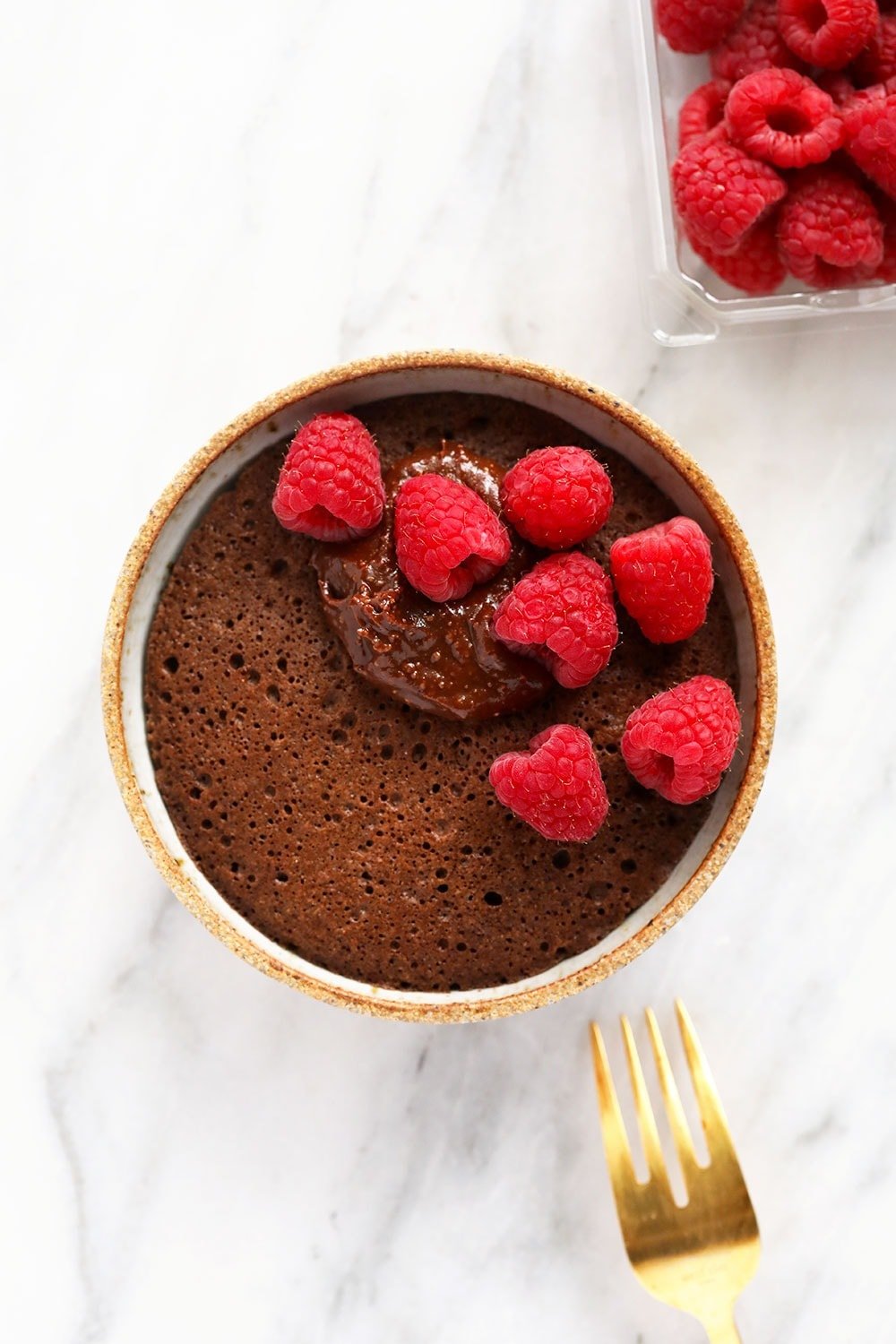 single-serve chocolate mug cake topped with fresh raspberries and homemade chocolate frosting