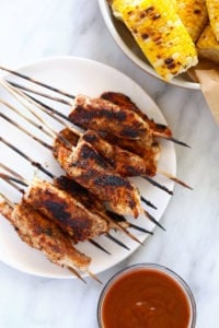 Chicken skewers served with corn on the cob.