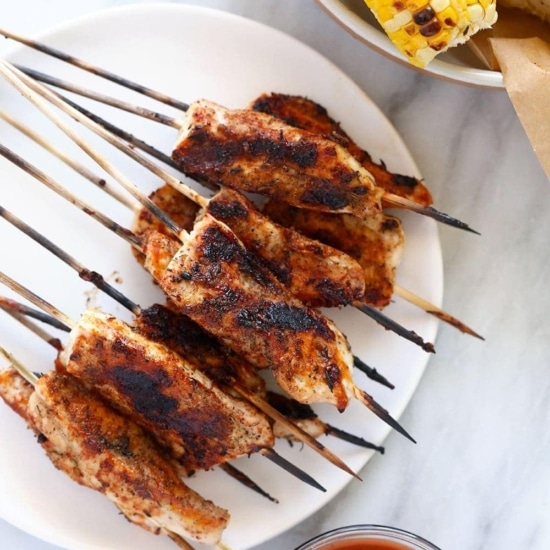 Chicken skewers served with corn on the cob.