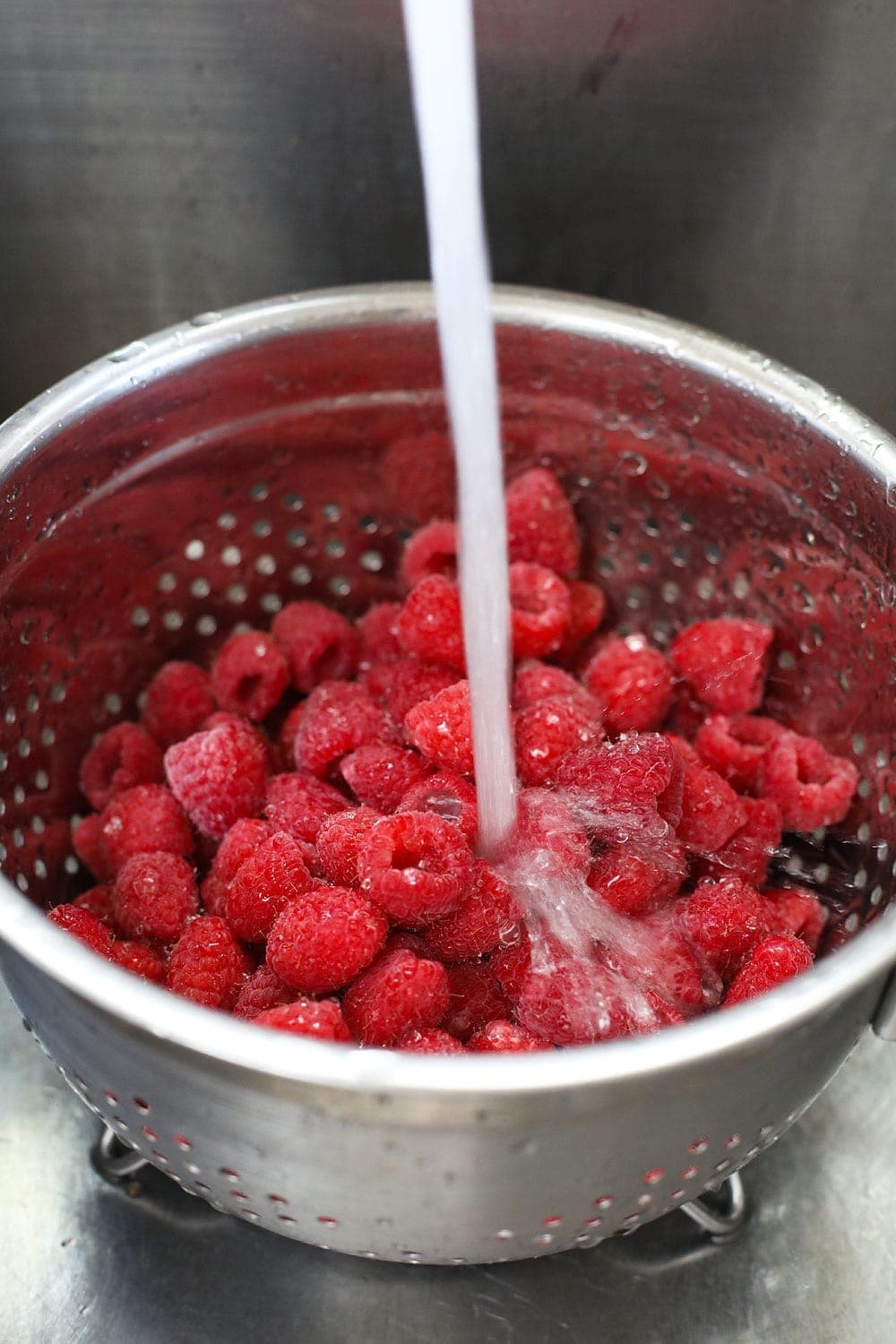 raspberries being washed in a colander