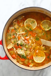 a pot of chicken soup with lemon wedges.