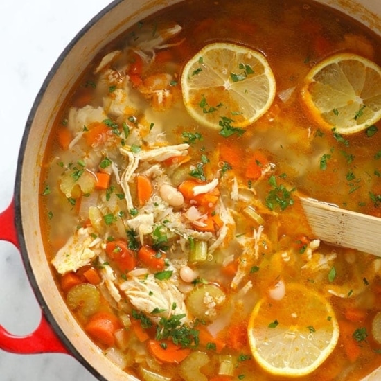 a pot of chicken soup with lemon wedges.
