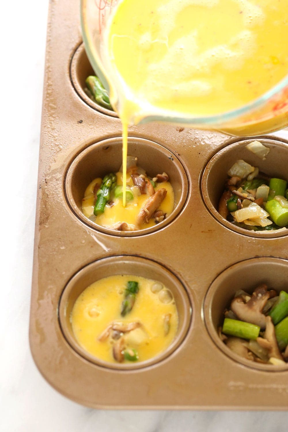 Pouring egg mixture into a muffin tin 