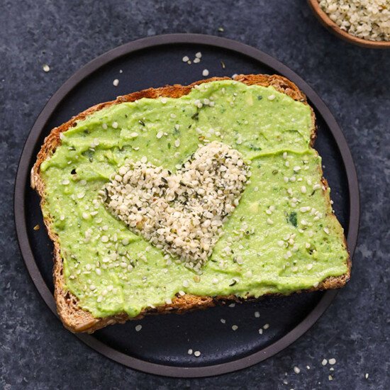 Heart shaped avocado toast with a spread on a plate.