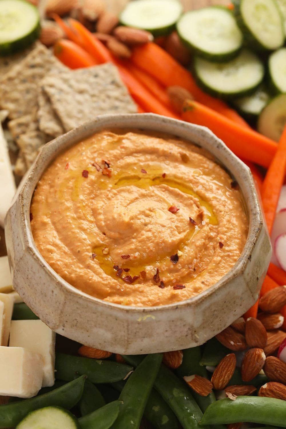roasted red pepper hummus surrounded by crackers, sliced veggies and crackers