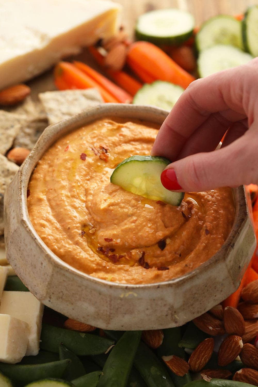 roasted red pepper hummus with a cucumber being dipped in it