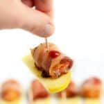 a person holding a bacon wrapped apple on a stick with honey