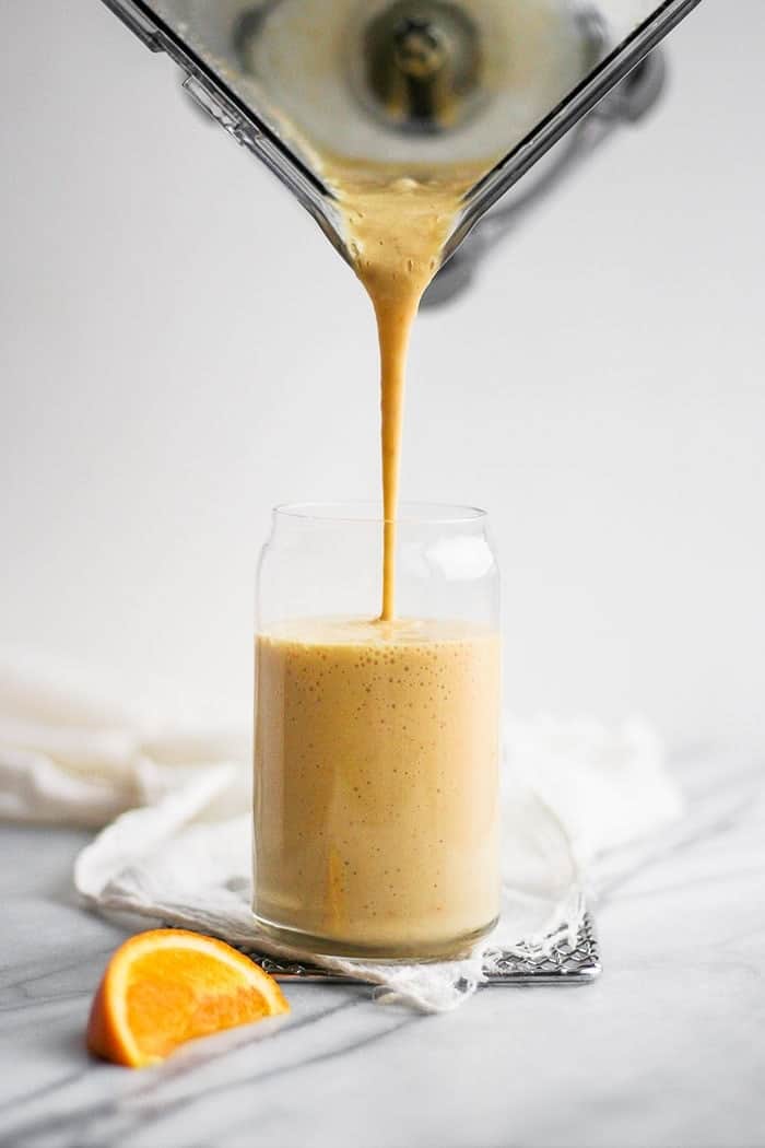 pouring orange smoothie into glass