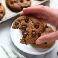 a hand holding a paleo cashew butter cookie with a bite taken out of it.