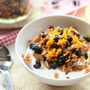 A healthy bowl of yogurt topped with granola and oranges.