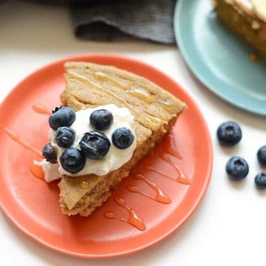 A breakfast cake with banana, blueberries, and whipped cream on a plate.