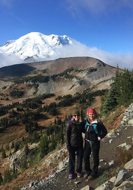 Two women hiking on a trail in Seattle with a mountain in the background.