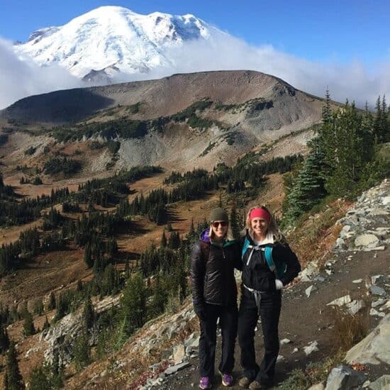Two women standing on a trail near Seattle with a mountain in the background.