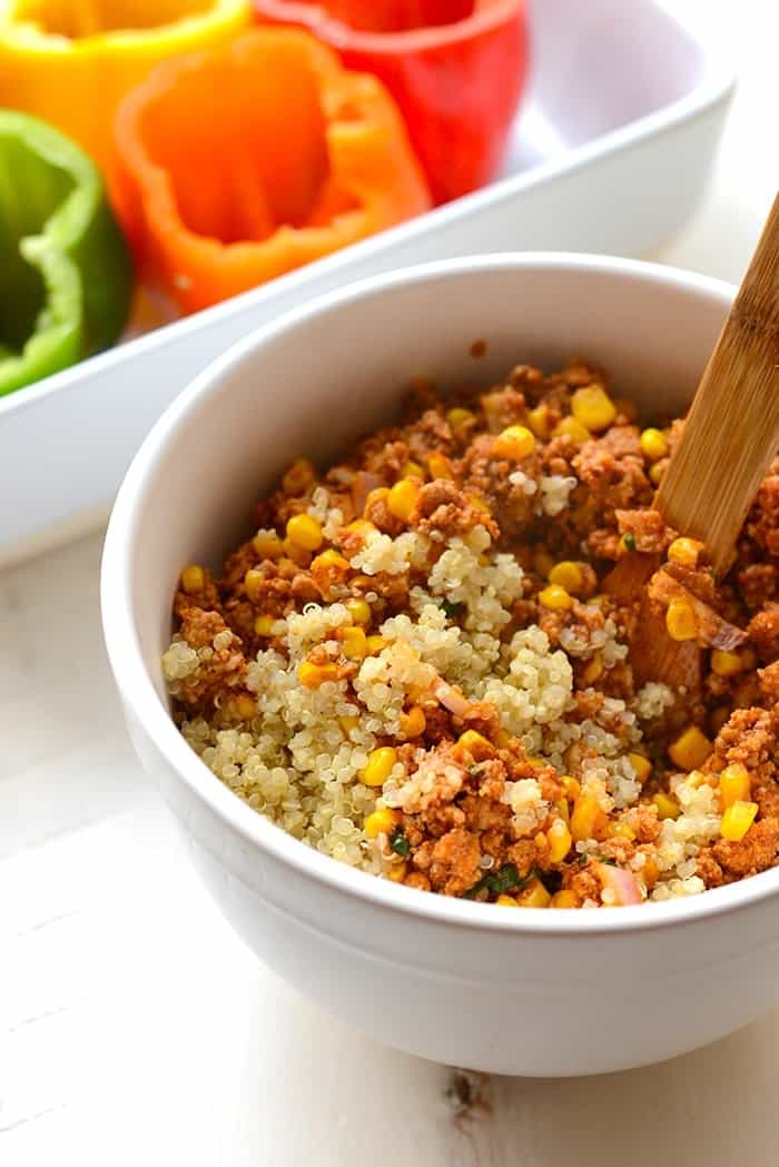 quinoa mixture for mexican stuffed peppers in white bowl with wooden spoon