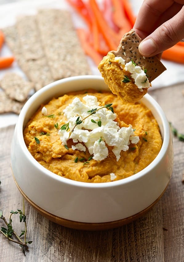 A person is dipping a cracker into a bowl of sweet potato hummus.