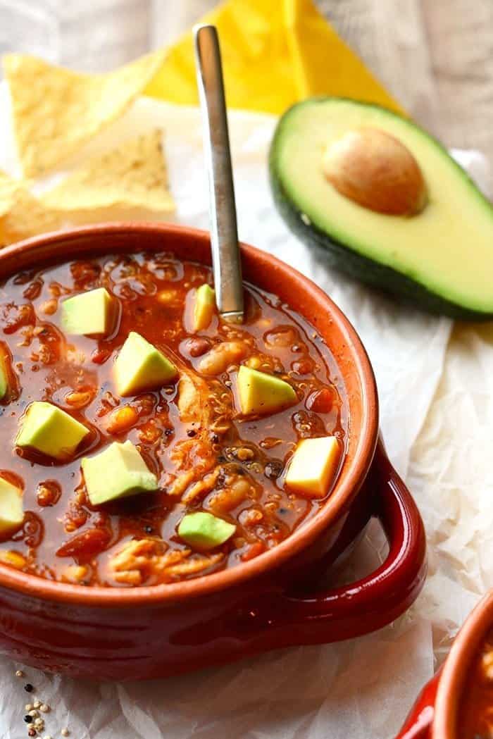 chicken enchilada soup in a bowl with sliced avocado