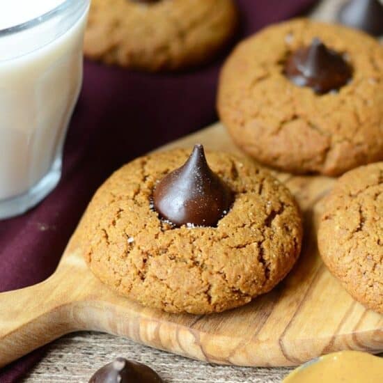 Peanut butter cookies on a cutting board paired with a glass of milk, featuring grain-free and peanut butter blossoms.