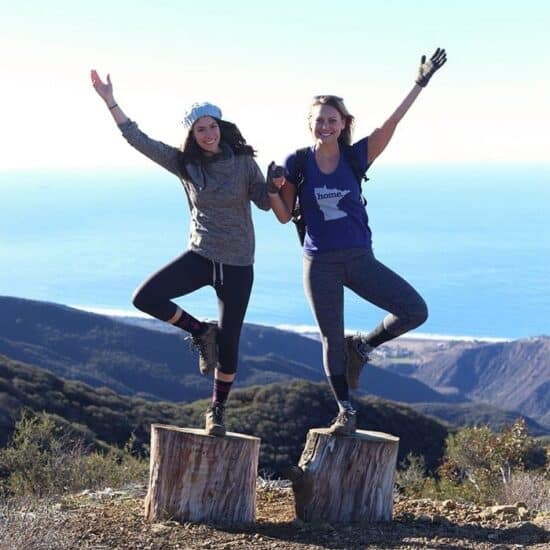 Two fitness enthusiasts from Wellfit Malibu balancing on a tree stump.