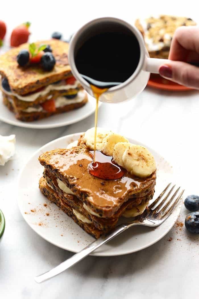 Stuffed french toast on a plate with banana slices and maple syrup poured on top.
