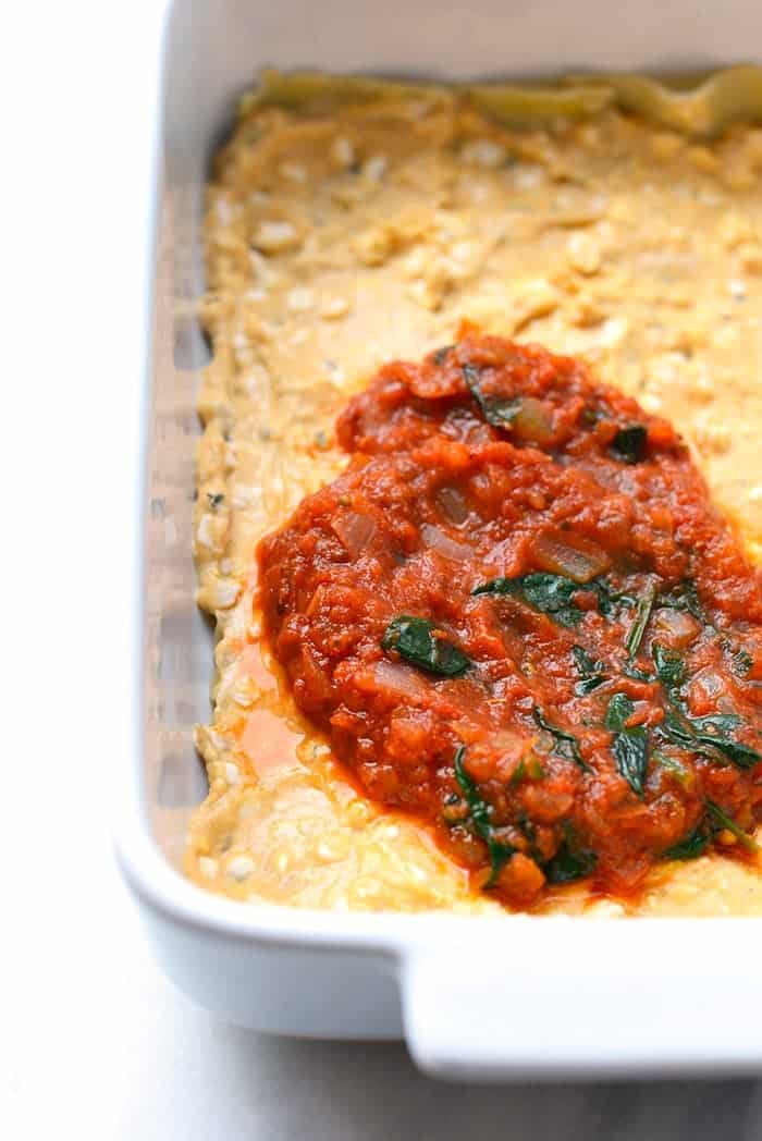sauce being spread on lasagna noodles for sweet potato lasagna