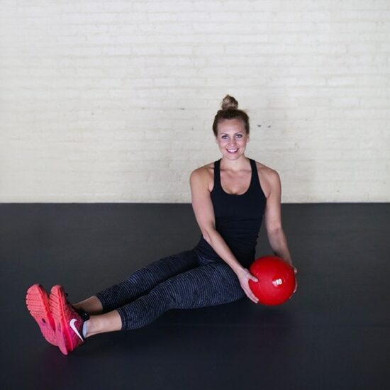 A woman engaging in a strength training workout on the floor with a red ball.