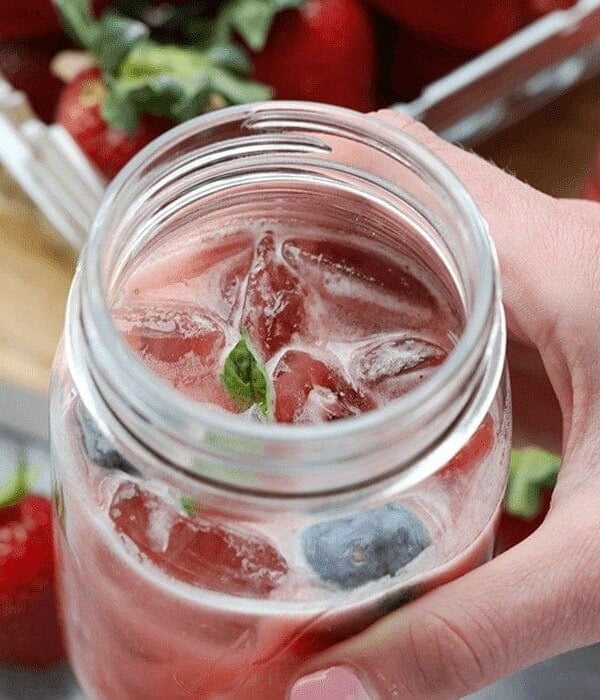 a hand holding a mason jar of strawberry lemonade Kombucha Mocktail.