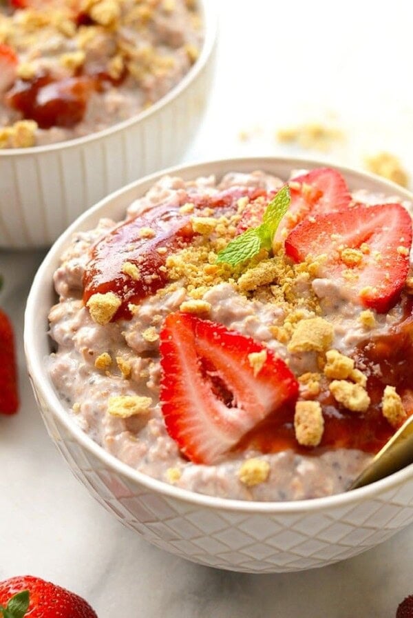 Two bowls of overnight oats with strawberries and granola, resembling strawberry cheesecake.