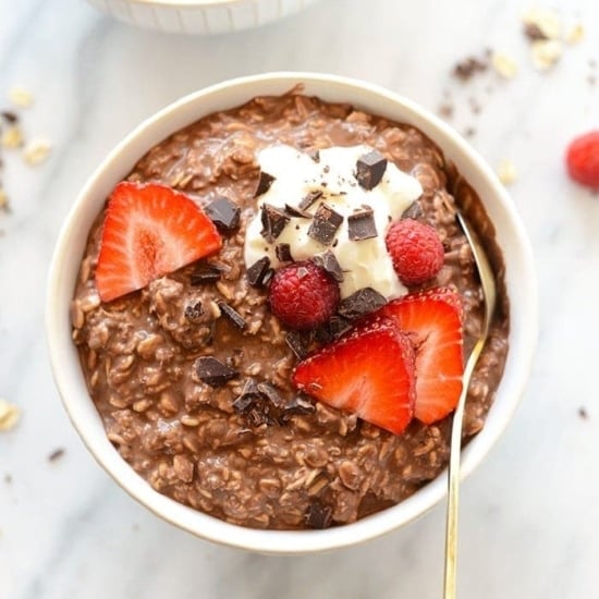 A bowl of chocolate oatmeal with strawberries and whipped cream.