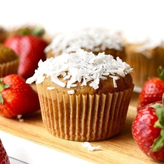 Blender coconut muffins with strawberries on a wooden cutting board.