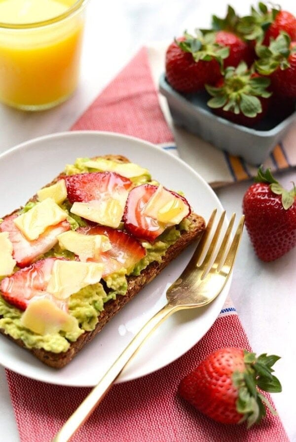White cheddar toast topped with avocado, strawberries, and a side of orange juice.
