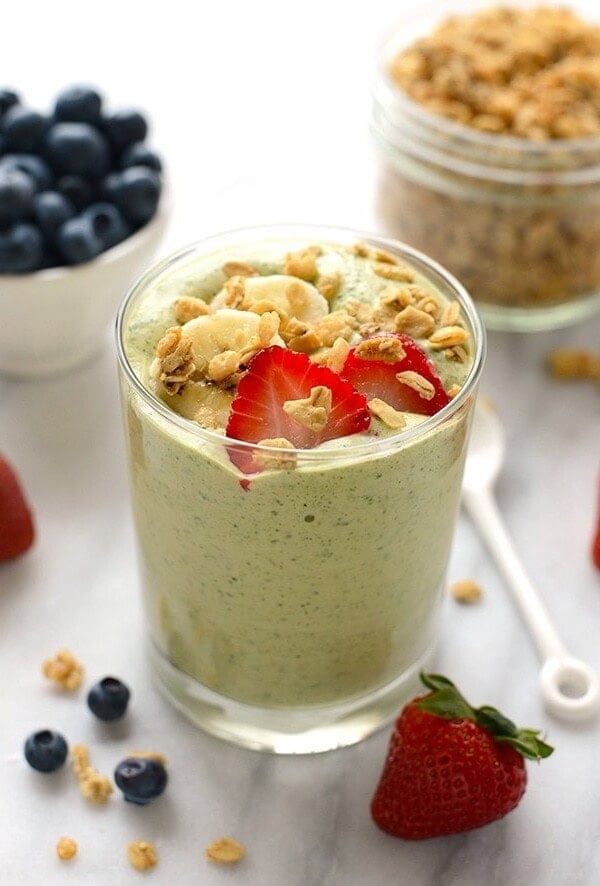 a spinach smoothie in a glass with berries and granola.