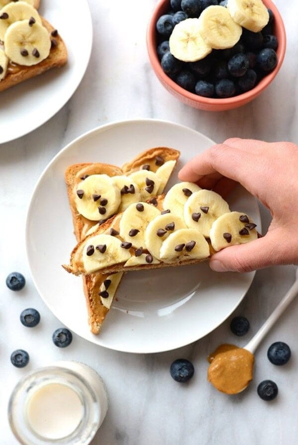 A person is holding a waffle with peanut butter, bananas and blueberries on it.