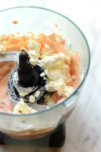 A food processor filled with roasted red pepper and goat cheese dip, featuring cream cheese and other ingredients.