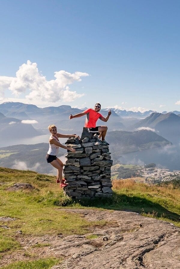 two people standing on top of a rock with mountains in the background.