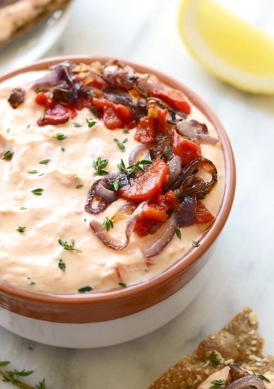 a bowl of skinny roasted red pepper and goat cheese dip with onions and tomatoes.