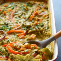 A curry quinoa casserole garnished with vegetables and served with a spoon.