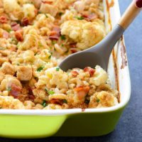 Cauliflower casserole with chicken and cheese in a green dish with a spoon.