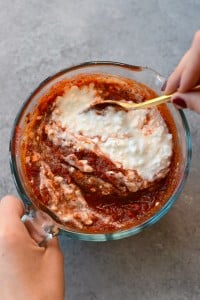 A person pouring sauce onto a Naked Spinach Quinoa Lasagna Casserole.