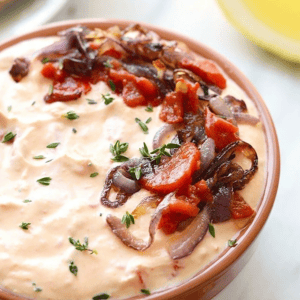A bowl of roasted red pepper and goat cheese dip with onions and tomatoes.