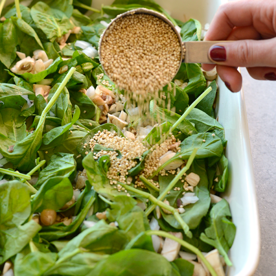 A person adds sesame seeds to a spinach salad.
