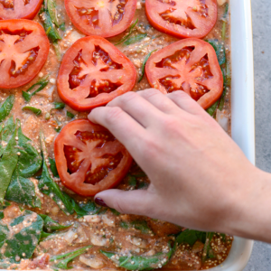 a person is removing tomatoes from a Naked Spinach Quinoa Lasagna Casserole.
