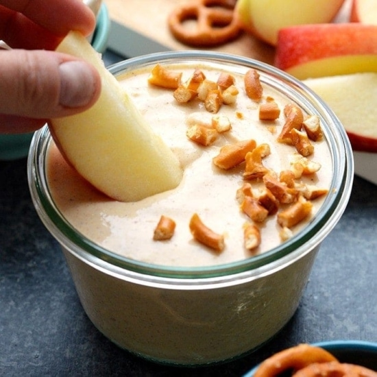 a person is dipping an apple into a bowl of pumpkin yogurt dip.