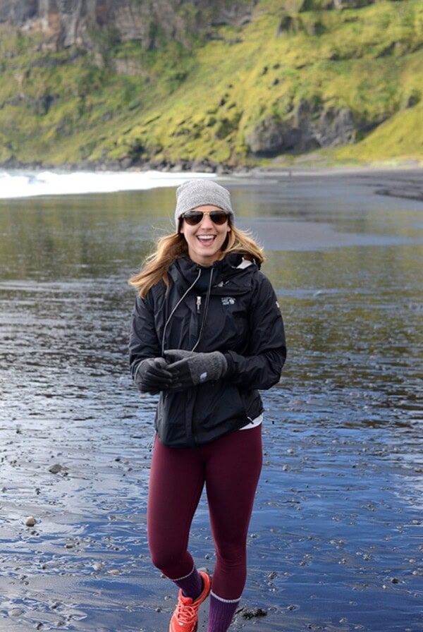 a woman standing on a black sand beach in iceland.
