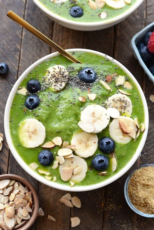 healthy green smoothie bowl topped with fruit and nuts and chia seeds